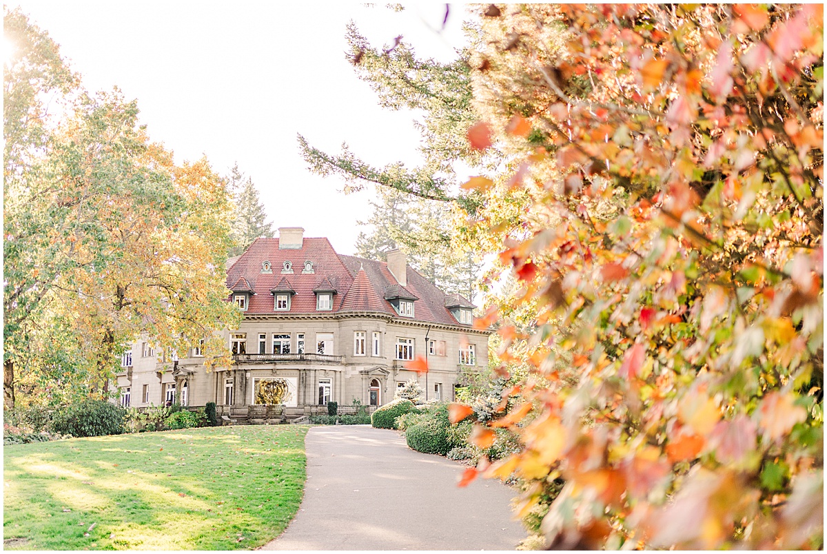 Pittock Mansion in Portland, Oregon surrounded by trees in the fall with orange and red leaves changing colors and a pathway leading up to the mansion